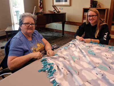 Nursing home resident and SDSU college student pose for the camera while working together on a fleece tie-blanket