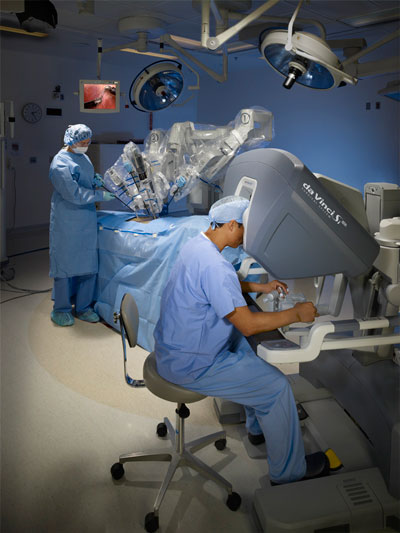 The new da Vinci robotic surgical system acquired by Brookings Health System will be used for a range of minimally invasive surgeries. Here a surgeon is sitting at the console, viewing HD video of the patient and using the fingertip controls. In the background, a patient lies under the patient side-cart where three interactive robotic arms transfer the surgeon’s movements.
