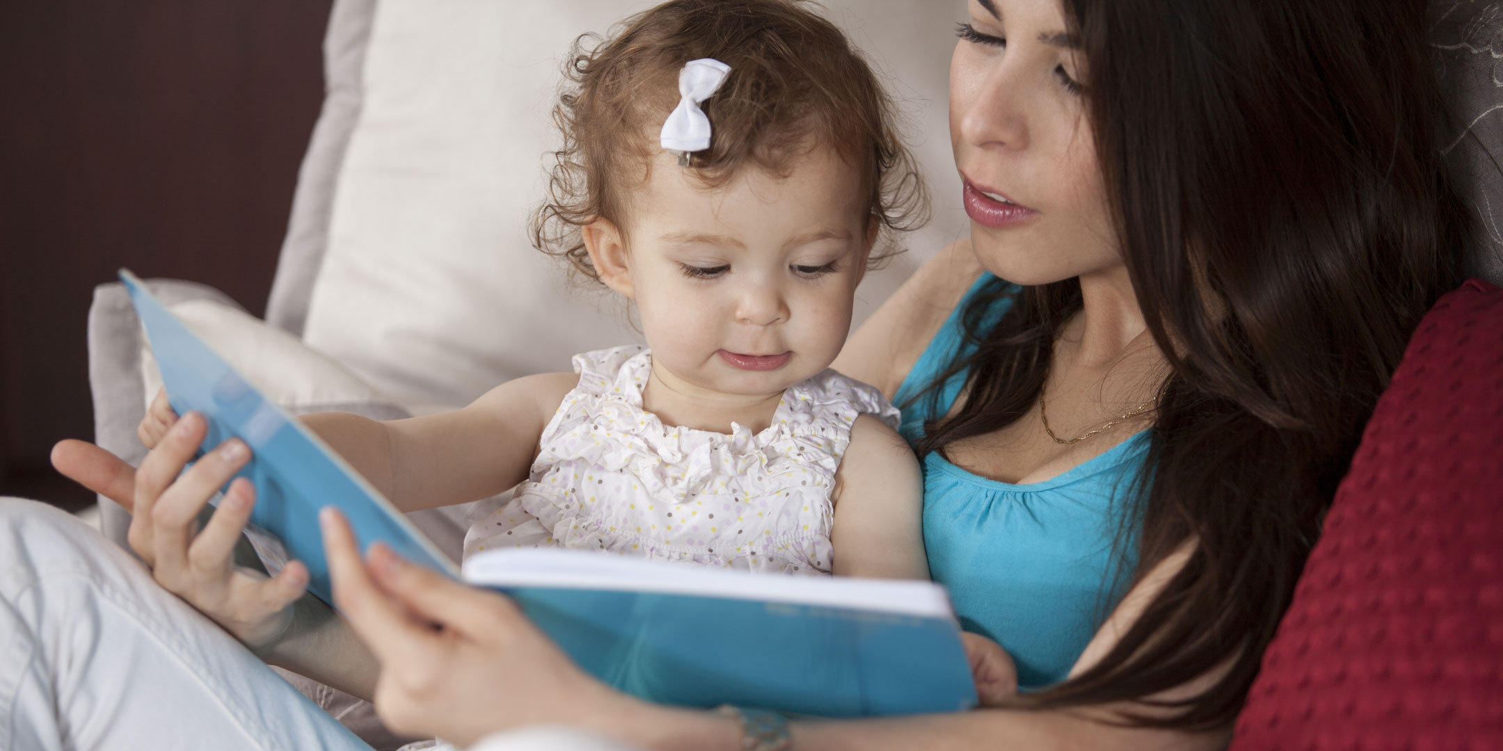 Tween girl reading to an infant girl that she is babysitting