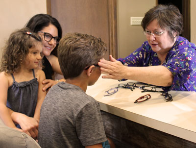Optician fitting glasses frames on a boy while mom and sister watch