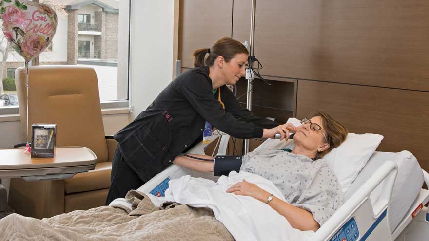Nurse checking a hospital patient's temperature while laying in bed. Get well balloon in background.