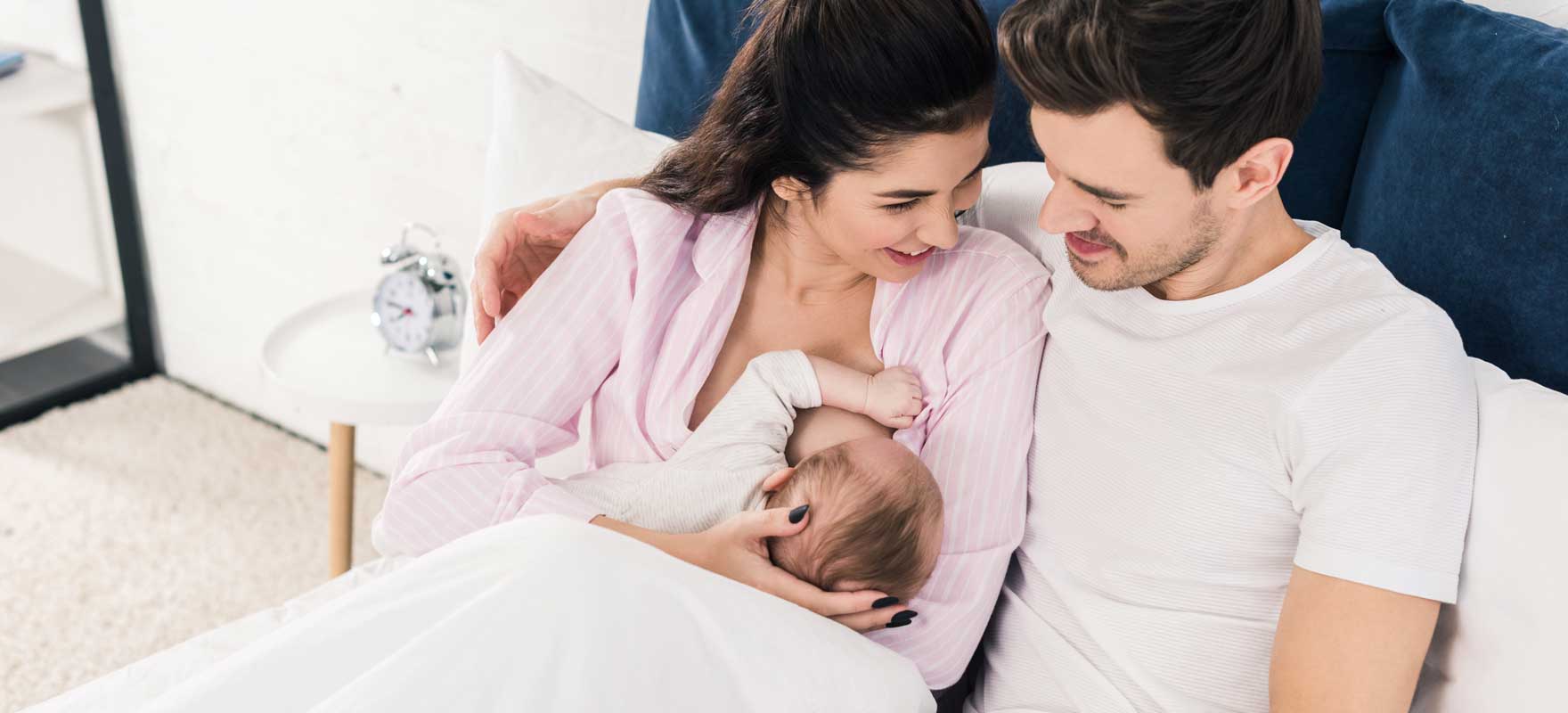 couple in bed together with woman nursing their baby while man supportively watches