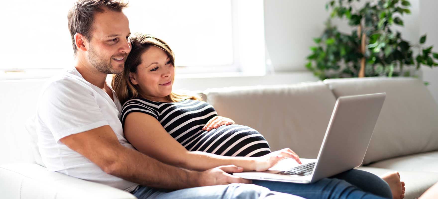 pregnant couple looking at a computer screen while sitting together on a couch