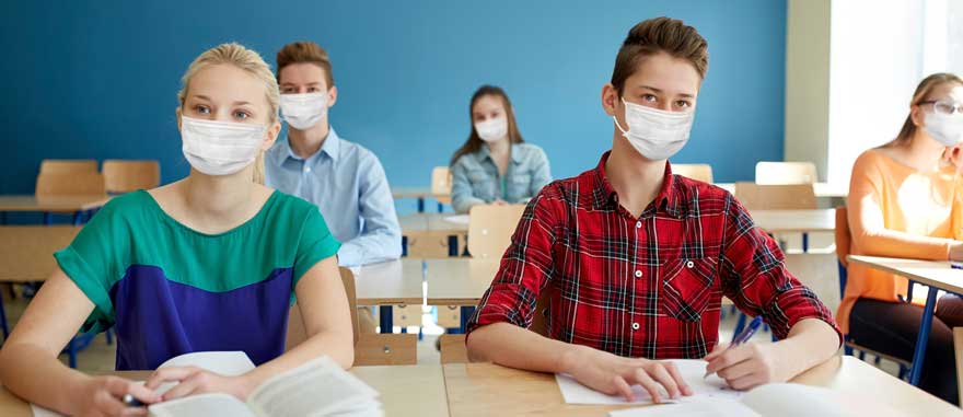A group of teenagers with masks sitting in class socially distanced from one another.