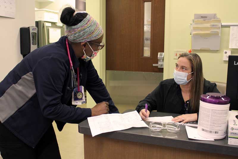 Night nurse Lindsey Thompson, RN, listens to patient care updates provided by day nurse Gladys Sterud, RN, during shift change on Brookings Hospital’s inpatient care unit. Team members like Thompson and Sterud have been working considerable overtime due to effects of the COVID-19 pandemic. Limited beds for patients in nursing homes and larger hospitals, the industry-wide healthcare workforce shortage, and the fear of what may possibly come next are severe stressors healthcare workers currently face. Brookings Health’s employees have started new programs to help peers cope with the strain and are asking the community to support Brookings Health System Foundation during the South Dakota Day of Giving next Tuesday. Monies raised will help fund resources for healthcare workers’ mental health and wellbeing.
