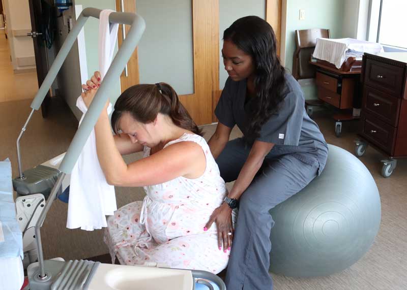 Doula helping a pregnant mother during labor and delivery by having her squat on the floor