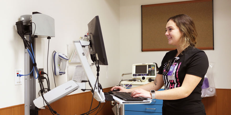 Emergency department health unit coordinator, Morgann, works on the computer inside a patient room