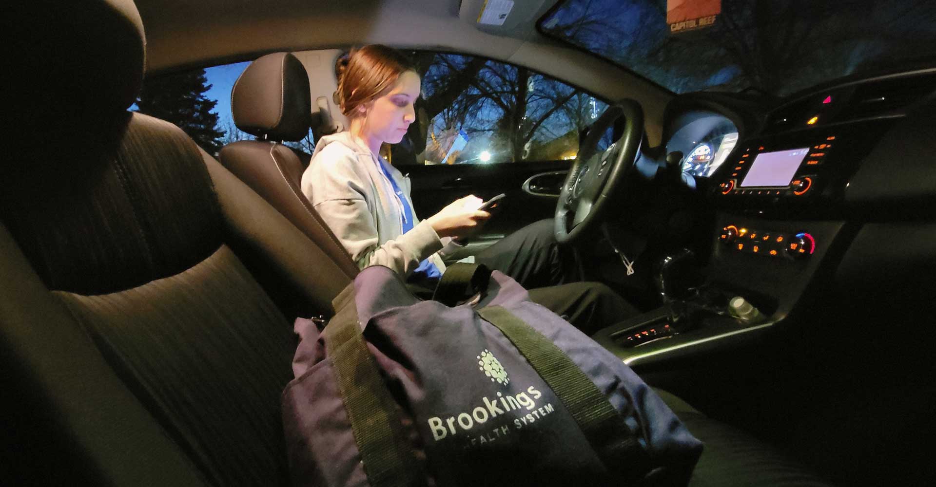 Hallie, a home health aide sitting inside her car, charting a patient visit on her cell phone
