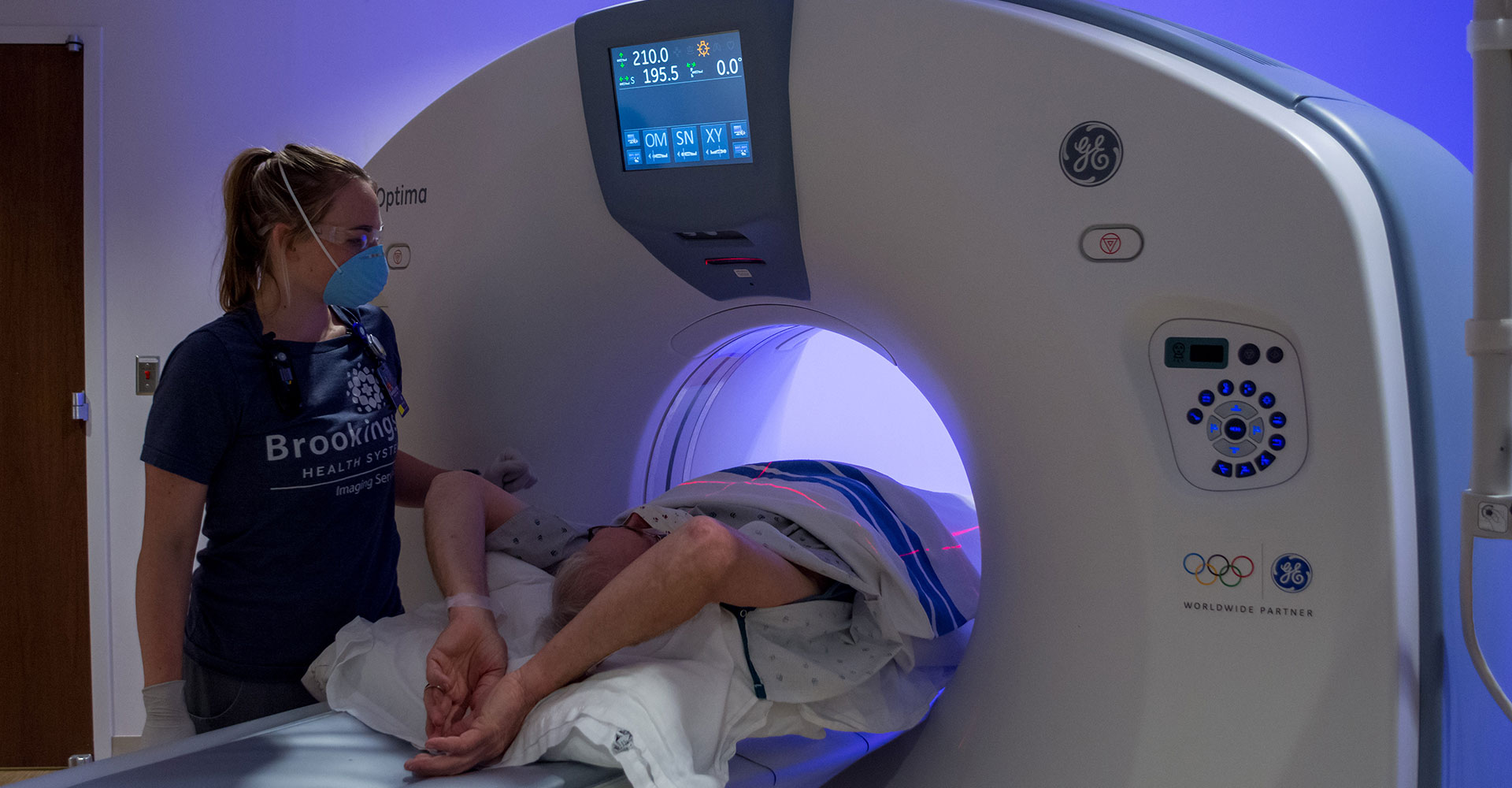 Patient getting a CT scan, assisted by a technologist with appropriate personal protective equipment
