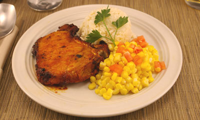 Herb baked pork chop plated with corn and rice