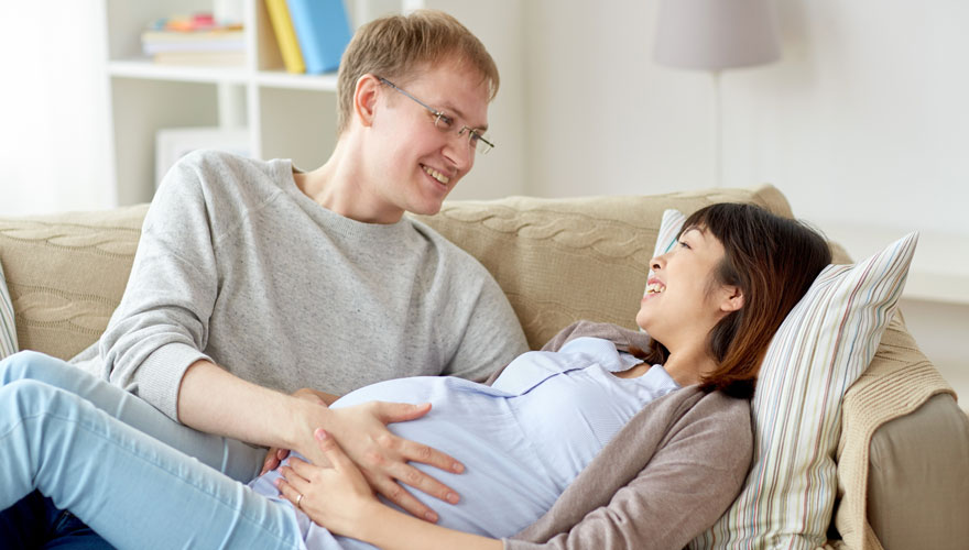 Expectant parents on couch with father feeling mother's pregnant stomach