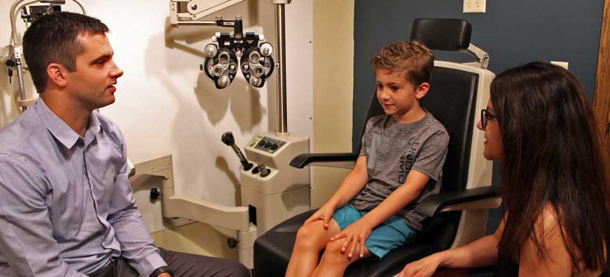Optometrist visiting with mother about a son's vision while son sits in the examination chair