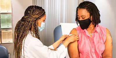 African American female care provider placing a bandage on the arm of an African American female patient after receiving a shot