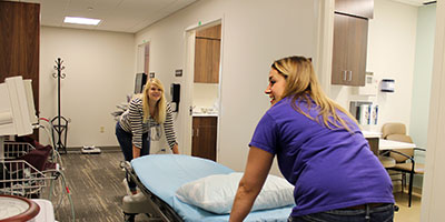 Outreach/Patient Services Representative Miah Badawi and Outreach Clinic Coordinator Jennifer Chandler, RN, move a bed in to one of the new outreach clinic exam rooms. Team members moved into the newly renovated portion of the original 1964 Brookings Hospital building last week. Care providers will start seeing patients in the remodeled spaces this week.