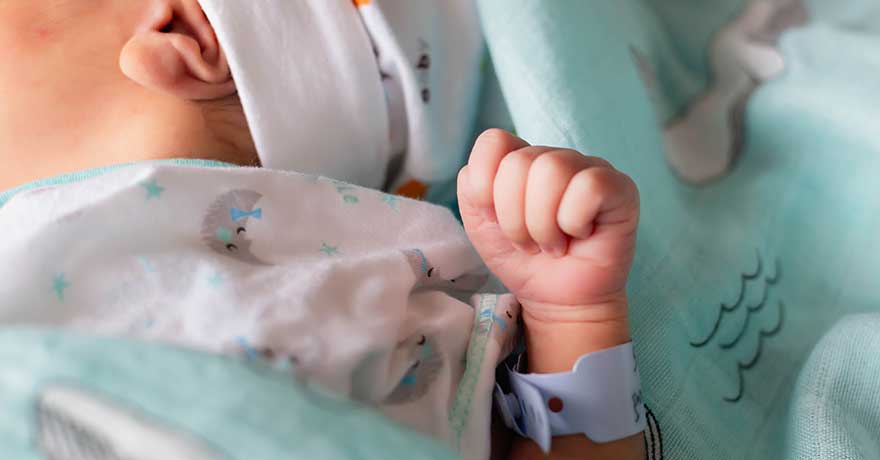 Upclose shot of tiny, braceleted hand of newborn baby held next to their little body and head